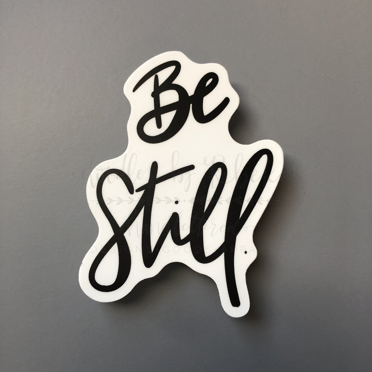 A white sticker with the phrase 'Be Still' written in a flowing black script font.