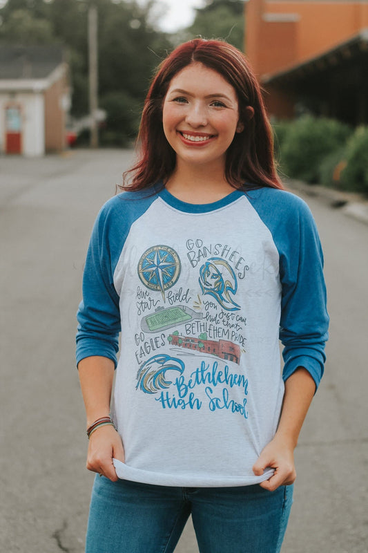 A person wearing a long-sleeved baseball tee with blue sleeves and white body, featuring hand-drawn lettering and designs related to Bethlehem High School.