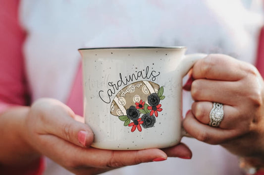 A person holding a white ceramic mug with 'Cardinals' text and a football graphic in red and gray.