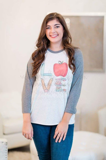 A person wearing a grey t-shirt with the word 'LOVE' and an apple graphic, paired with blue jeans.