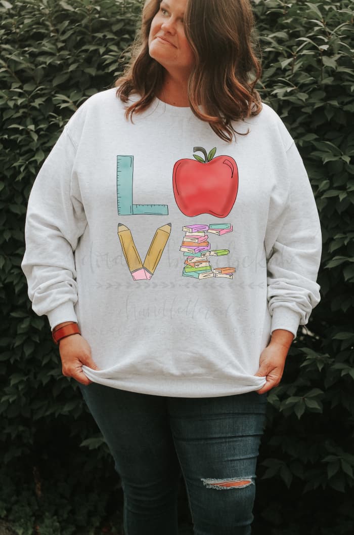 Doodles by Rebekah teacher-themed "LOVE" raglan shirt with whimsical hand-drawn school supply illustrations.