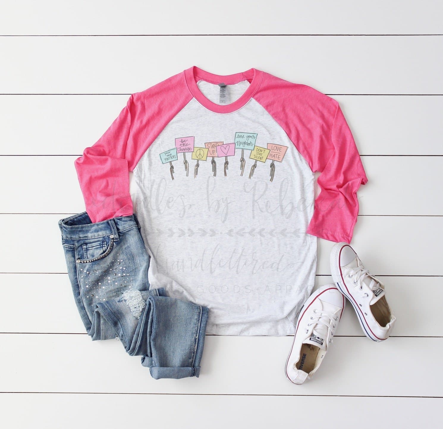 Flat lay of a pink and white raglan shirt with "Be the Change" and "Love Your Neighbor" signs, jeans, and white sneakers.